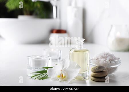 Huiles essentielles, sel de mer, pierres de spa et fleurs d'orchidées sur table blanche dans la salle de bains Banque D'Images