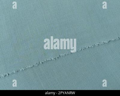Bord déchiré de tissu de laine fine en vert ou bleu. Fils lâches au bord d'un morceau de textile. Gros plan. Fond tissé. Couleur pastel vert calme Banque D'Images