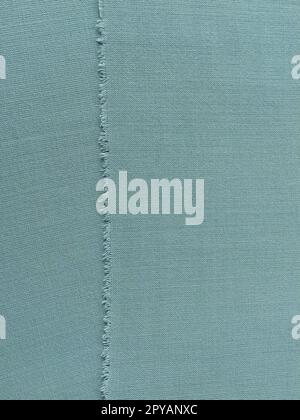 Bord déchiré de tissu de laine fine en vert ou bleu. Fils lâches au bord d'un morceau de textile. Gros plan. Fond tissé. Couleur pastel vert calme Banque D'Images