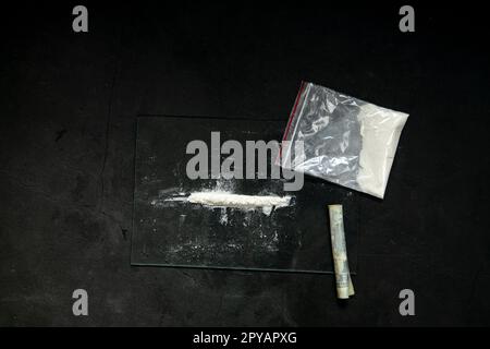 Lignes de poudre de cocaïne, billets roulés et drogues dans une poche de sac en plastique sur fond de verre noir, vue du dessus. Notion de toxicomanie Banque D'Images