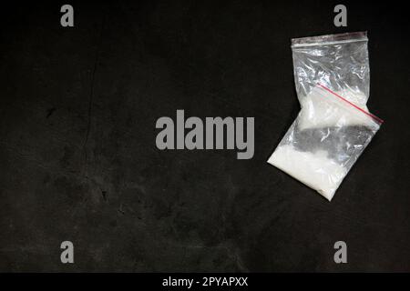 Lignes de poudre de cocaïne, billets roulés et drogues dans une poche de sac en plastique sur fond de verre noir, vue du dessus. Notion de toxicomanie Banque D'Images