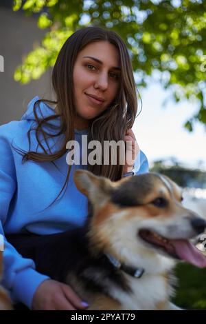 Portrait d'une jolie jeune femme assise sur un banc avec un chien de corgi. Un propriétaire d'animal de compagnie gai tenant Pembroke Welsh Corgi sur des longueurs en plein air Banque D'Images