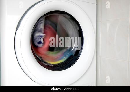 Gros plan de la porte du lave-linge avec vêtements multicolores tournant à l'intérieur avec espace de copie lave-linge et sèche-linge design blanc moderne Banque D'Images