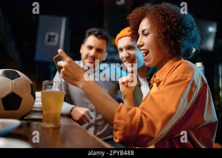 Des amis joyeux s'amusent à regarder un match de football sur smartphone au bar sportif Banque D'Images