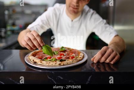 Chef pizzeria décorant pizza avec feuilles d'origan fraîches Banque D'Images