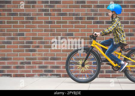 Vue de profil d'un garçon dans un casque, à vélo sur le trottoir contre le fond du mur de briques Banque D'Images