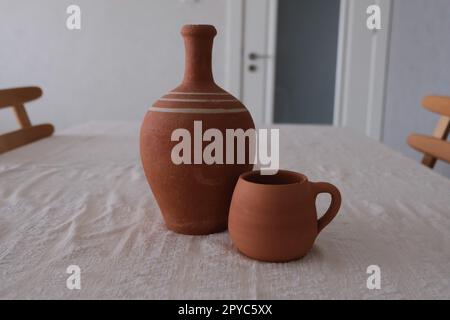 Vue de face d'un ancien pichet en céramique antique non peint sur une nappe traditionnelle. Pichet en argile et tasse pour boire du vin ou de l'eau. Banque D'Images