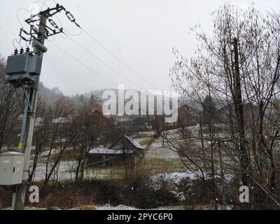 Ligne électrique à la campagne. Danger pour la vie si vous rampez ou touchez avec vos mains. Montagnes et collines en Bosnie-Herzégovine. Campagne avec maisons privées à deux étages. Gros flocons de neige blancs Banque D'Images