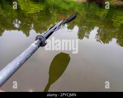 Une pagaie en kayak surélevé au-dessus d'une rivière boisée avec des arbres réfléchis dans l'eau. Banque D'Images