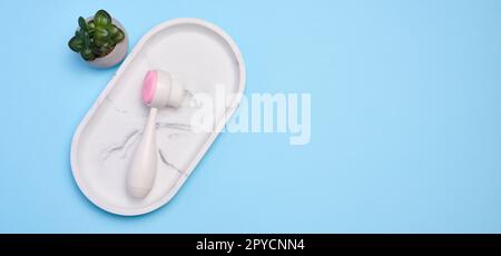 Brosse à récurer visage en plastique blanc sur un fond bleu, outil cosmétique. Vue de dessus Banque D'Images