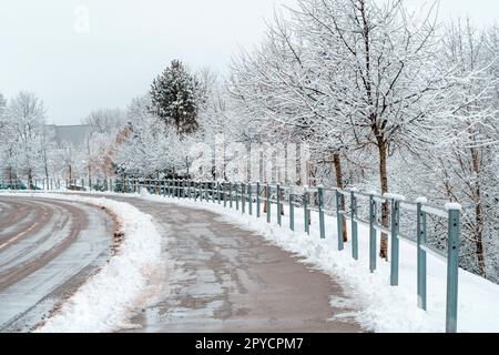 Route asphaltée et trottoir recouverts de neige mouillée et de boue Banque D'Images