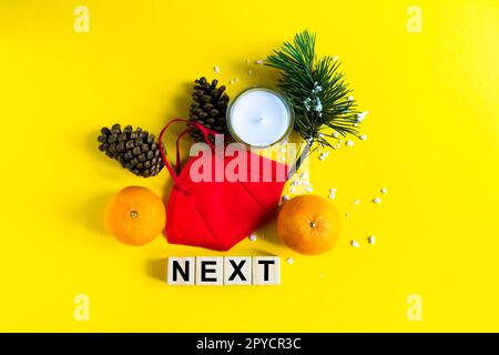 Les mandarines se trouvent dans un masque médical parmi les branches de l'arbre de Noël, mot Suivant cubes en bois Banque D'Images