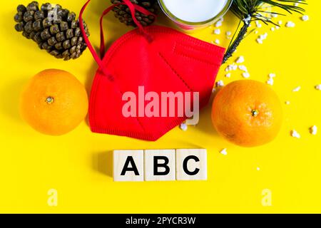 Les mandarines se trouvent dans un masque médical parmi les branches de l'arbre de Noël, mot ABC cubes en bois Banque D'Images