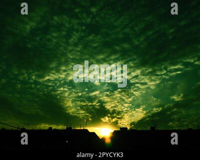 Coucher de soleil sur les toits de la ville. Nuages dans le ciel du soir. Les rayons du soleil transpercent les nuages. Vert - couleurs jaunes du ciel et des nuages. Beau paysage. Le soleil se couche Banque D'Images