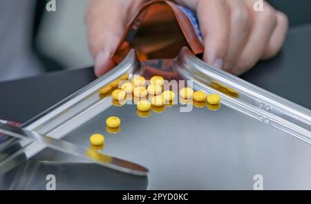 Focalisation sélective sur les comprimés jaunes pilules sur plateau inoxydable avec main floue du pharmacien ou du technicien en pharmacie comptant les pilules dans un sac à fermeture éclair en plastique. La médecine de prescription. Les soins médicaux. Banque D'Images