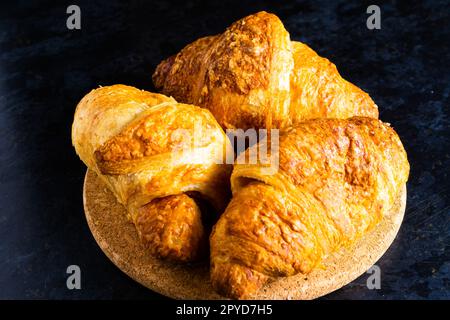 Croissant français fraîchement soutenu brillant dans les rayons du soleil du matin, fond sombre, cuisine Banque D'Images