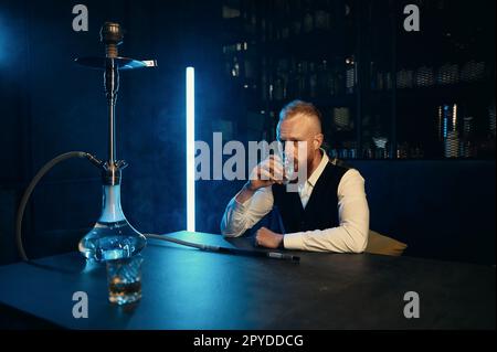 Un homme élégant en costume boit du whisky au bar Hookah Banque D'Images