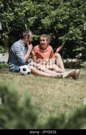 épaté adolescent assis près du ballon de football avec le père dans le parc vert d'été, image de stock Banque D'Images