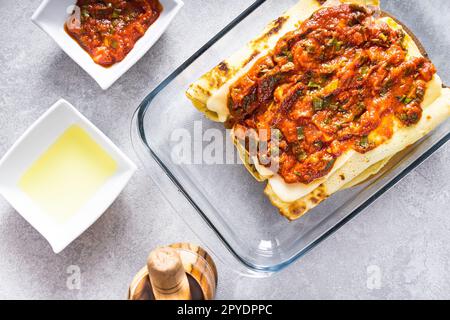 Délicieux crêpes à la viande dans un bol en verre, avec œufs, blé, huile d'olive, sauce tomate et une nappe à carreaux en arrière-plan. Banque D'Images