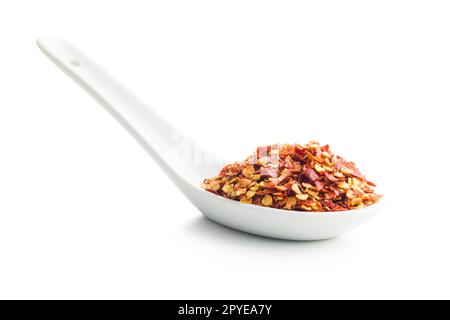 Sécher les flocons de piment dans une cuillère en céramique. Poivrons rouges écrasés isolés sur fond blanc. Banque D'Images