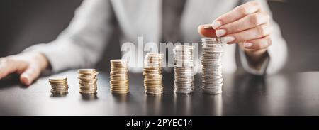 Femme assise à la table et mettant la pièce de monnaie sur la plus grande pile de l'argent. Banque D'Images