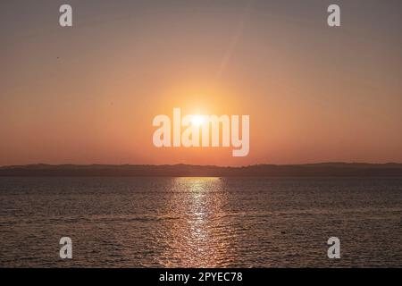 Beau coucher de soleil sur le magnifique lac de Garde en Italie, avec le soleil se reflétant sur l'eau calme Banque D'Images