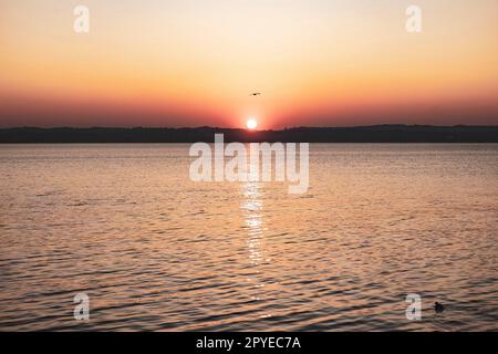 Beau coucher de soleil sur le magnifique lac de Garde en Italie, avec le soleil se reflétant sur l'eau calme Banque D'Images