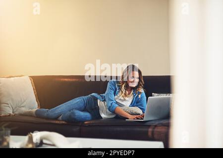 La vie est tellement plus facile quand vous vous détendez. une jeune femme détendue utilisant un ordinateur portable sur le canapé à la maison. Banque D'Images