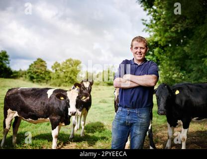 La maison est où sont mes vaches. Portrait d'un agriculteur mâle debout avec ses bras plié sur sa ferme laitière. Banque D'Images