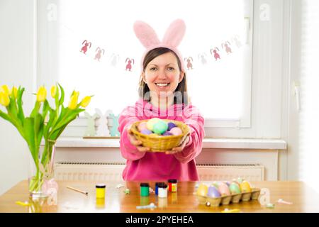 Portrait d'une femme souriante et heureuse portant des oreilles de lapin et tenant des œufs de Pâques colorés dans le panier. Banque D'Images