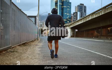 Fitness, homme noir et marche dans la rue de la ville après la course, l'exercice et la séance de gym avec un sweat à capuche la nuit. Dos d'un athlète masculin dans Miami urbain pour une marche et un entraînement cardio avec un sac de sport Banque D'Images