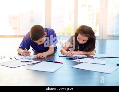 Laissez-les toujours être libres de créer. deux jeunes enfants s'allonger sur le sol et colorer en images dans leurs livres de coloriage à la maison. Banque D'Images