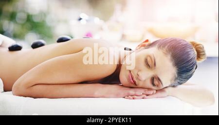 Vos maux vont naturellement s'éloigner. une jeune femme reçoit un massage aux pierres chaudes dans un spa. Banque D'Images