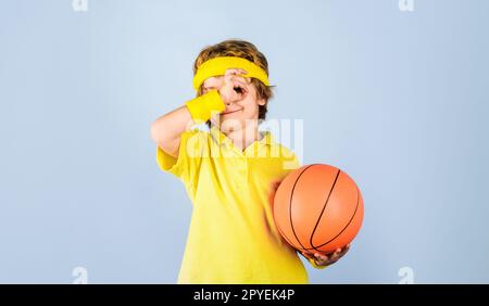 Petit ballon de base. Un enfant souriant avec un ballon de basket-ball montrant un signe ok, un excellent symbole. Sport garçon dans des vêtements de sport avec ballon de basket-ball. Sport Banque D'Images