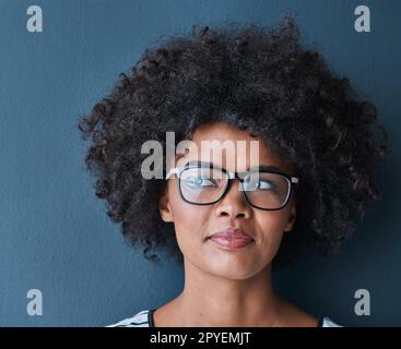 Je pense que je vais aller avec ça... photo en studio d'une jeune femme attrayante portant des lunettes et ayant l'air réfléchie sur un fond bleu. Banque D'Images