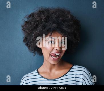 Parfois, vous avez juste à laisser sortir la bêtise. Portrait en studio d'une jeune femme séduisante collant sa langue sur un fond bleu. Banque D'Images