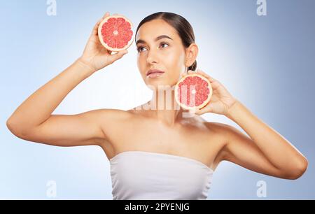 Femme, beauté et soins de la peau naturels avec pamplemousse, lueur rayonnante et esthétique saine par fond bleu. Modèle, brillance de la peau et fruits pour le bien-être, les soins personnels et la santé cosmétique par fond de studio Banque D'Images