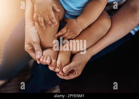 Petits orteils et petits pieds. Gros plan d'un homme méconnaissable tenant ses pieds d'enfant tout en étant assis sur un canapé à la maison pendant la journée. Banque D'Images