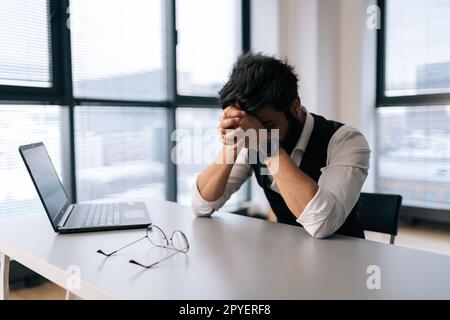 Un employé indien surtravaillé se sentant triste après le chômage de l'entreprise, assis au bureau se sentant stressant à craindre de perdre son emploi. Banque D'Images