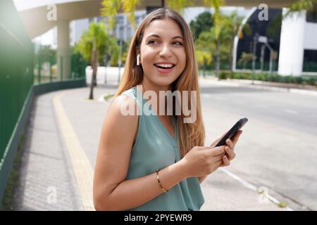 Belle fille brésilienne utilisant des écouteurs sans fil pour écouter de la musique dans la rue de ville Banque D'Images