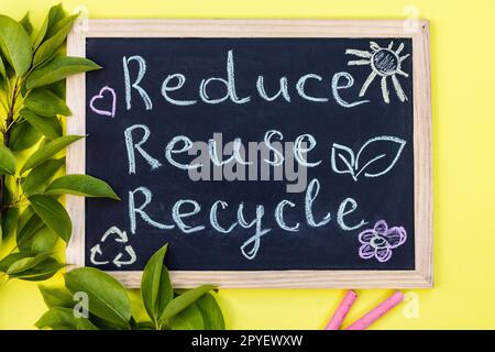 Tableau de craie Reduse Reuse Recycle signe sur fond jaune avec des feuilles vertes et des morceaux de craie. Vue de dessus. Banque D'Images