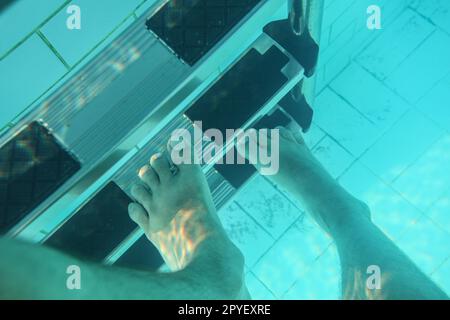 Photo sous-marine, l'homme marchant sur les pieds des escaliers de la piscine. Banque D'Images