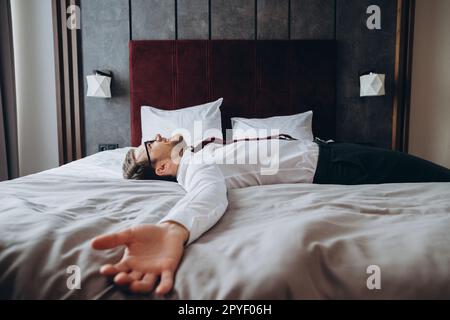 Homme d'affaires épuisé reposant sur le lit après un long vol d'air, décalage horaire. Homme en costume d'affaires allongé avec les bras étirés sur le matelas dans la chambre d'hôtel. Banque D'Images