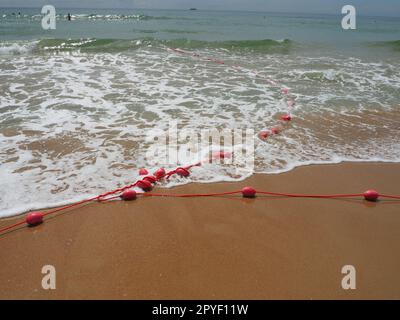 Bouées sur une corde dans l'eau de mer. Les bouées de sauvetage sont des dispositifs de retenue roses pour alerter les gens de la profondeur de l'eau. Sauvetage de la noyade. Délimitant un lieu sur une plage de sable entre les hôtels. Vague avec des bulles Banque D'Images