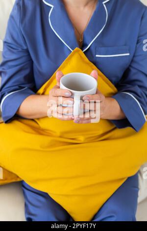 Femme en gros plan dans un confortable pyjama reposant sur un canapé à la maison et boissons thé ou café - bien-être et confort matin concept Banque D'Images