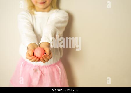 Les mains des enfants tiennent un œuf de Pâques rose. Joyeuses Pâques. Préparation pour Pâques et le printemps. Banque D'Images