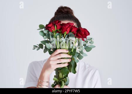 Arrêtez-vous et sentez les roses. Photo studio d'une femme méconnue couvrant son visage de fleurs sur fond gris. Banque D'Images