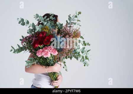 Il n'y a rien de plus beau qu'un bouquet. Photo en studio d'une femme méconnue tenant des fleurs sur un fond gris. Banque D'Images