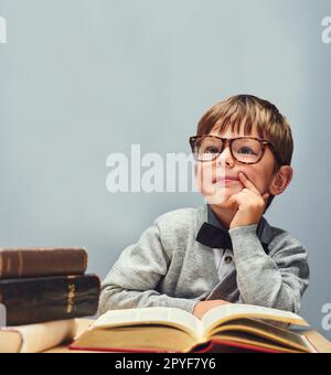 L'avenir appartient aux curieux. Studio photo d'un petit garçon intelligent lisant des livres et regardant réfléchi sur un fond gris. Banque D'Images