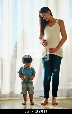 La technologie sans fil est un grand baby-sitter. une femme enceinte regardant son petit garçon pendant qu'il joue avec un smartphone. Banque D'Images